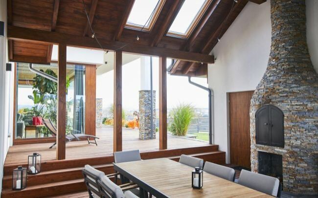Projekt dużego domu w Nowym Sączu obejmuje przestrzeń gilową pod zadaszeniem wiatą z piecem opalanym drewnem z kamienia łupek z drewnianą podłogą
